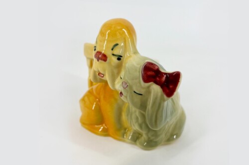 Glossy ceramic figurine showing a yellow-clad person beside a light-colored elephant with red inner ears, both posed together as a statue.