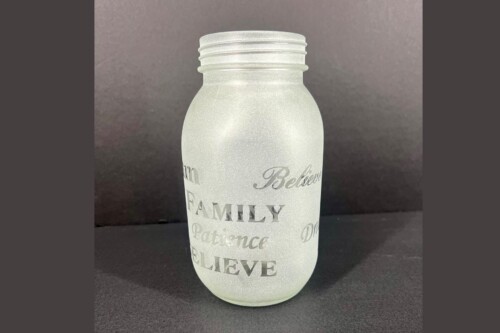Frosted glass bottle with printed inspirational words like Believe, Family, and Patience in silver script against a dark background.
