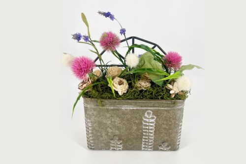 Metal decorative planter with a mixed flower arrangement including pink globe thistles, cream roses, white fluffy blooms and green foliage.
