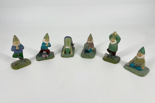 Six glittery gnome figurines with pointed hats on grassy bases, posed in a gentle arc on a white background (various gestures).