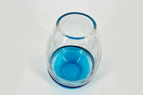Top-down view of a clear glass with bright blue liquid pooled at the bottom, seen from above.