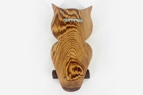 Back view of a carved wooden cat-head sculpture showing prominent wood grain and a metal mounting plate on the neck, mounted on a stand.