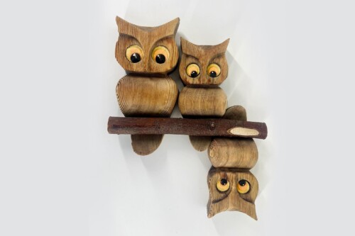 Row of carved wooden owls stacked along a dark branch, with large yellow eyes.