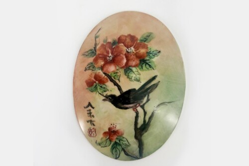 Oval wooden plaque with a hand-painted red flower bouquet on a branch and a black bird, against a pale background, with Chinese characters nearby.