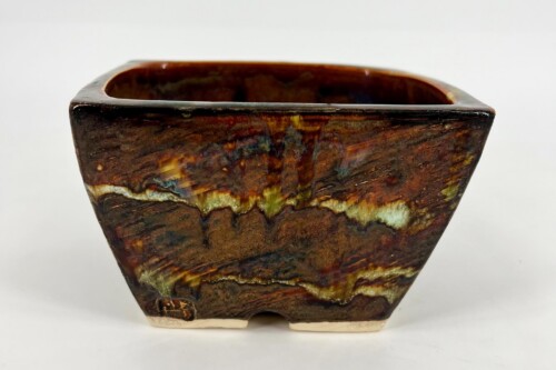 Close-up of a dark glazed ceramic vase with brown marbled glaze and a light-colored foot seen from the side.