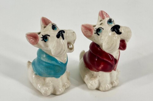 Two white ceramic dogs with blue and red scarves, facing each other on a white surface.