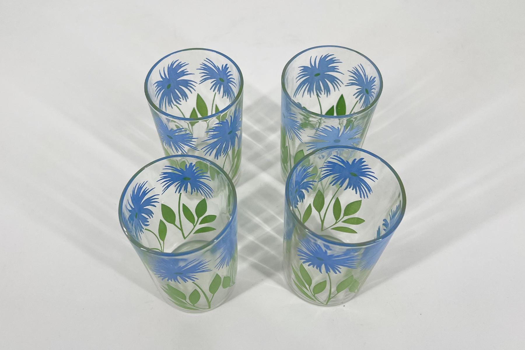 Four tall glasses with blue floral pattern and green leaves, viewed from above on a white surface.