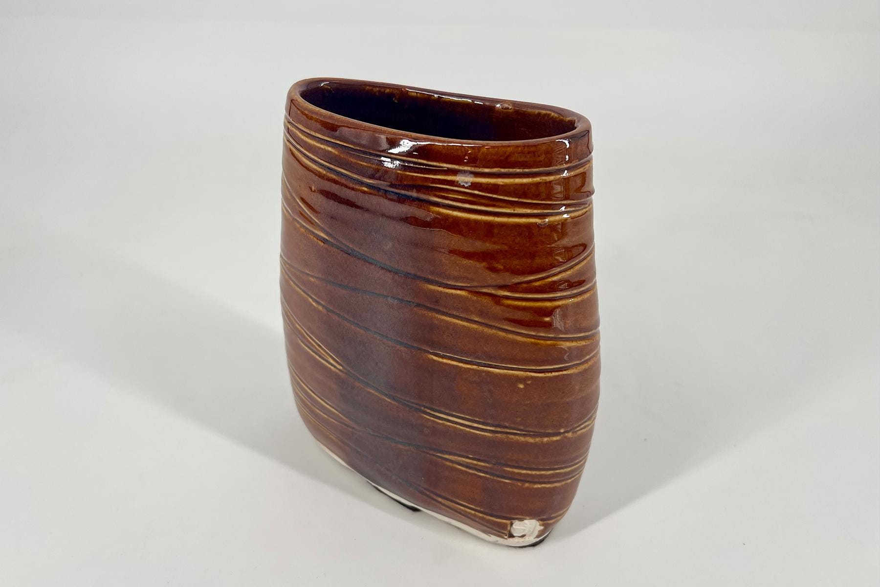 Brown glossy ceramic vase with diagonal ridges, empty interior, on a white background.
