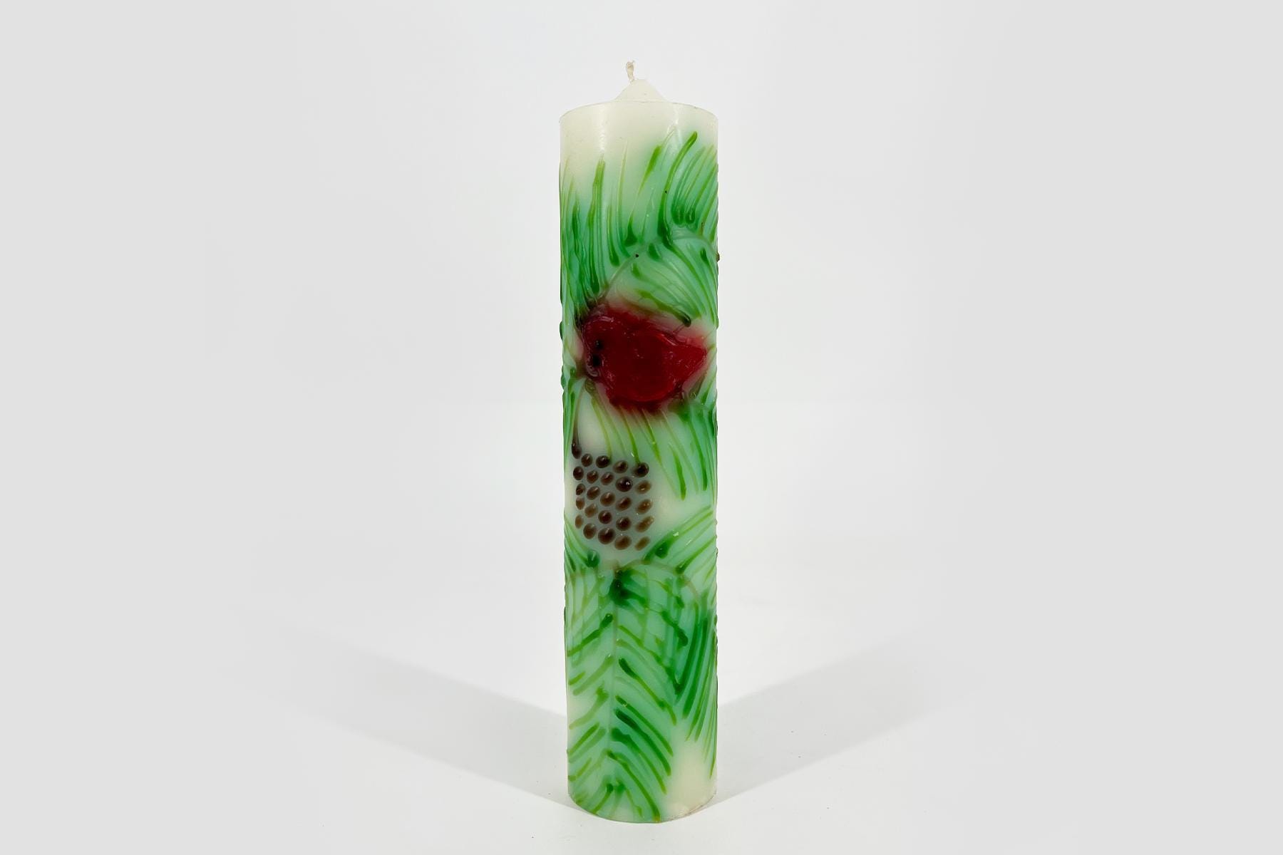 Tall white pillar candle with green marbling and a red central accent, set against a light background