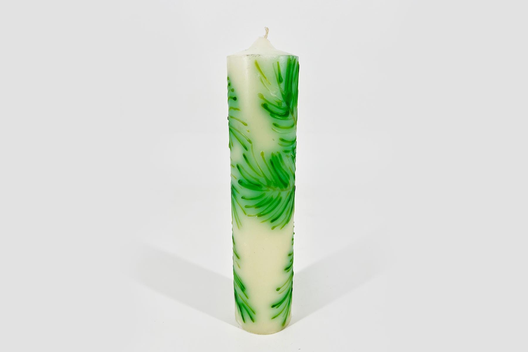Tall white pillar candle with green swirling marbling pattern on a light background, unlit and decorative.