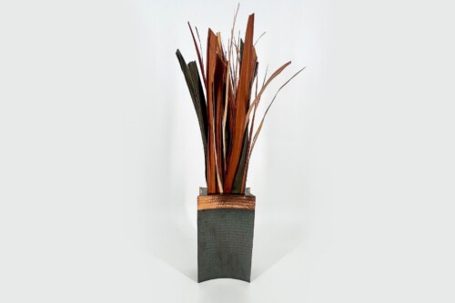 Abstract wooden sculpture with tall brown and orange slats arranged in a textured dark-green vase; decorative art piece.