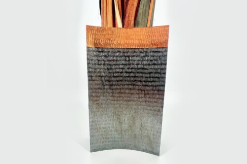Tall textured vase with a copper-to-charcoal gradient, holding dried plant stems at the top.