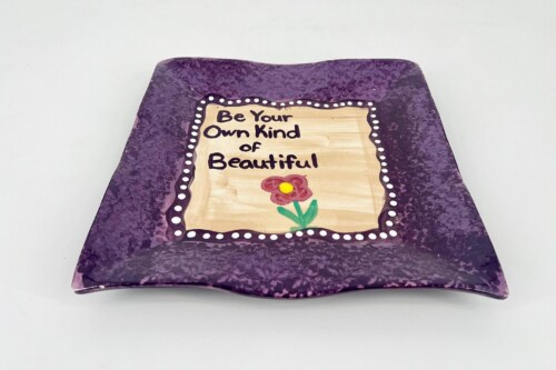 Purple decorative cake with a beige center reading 'Be Your Own Kind of Beautiful' and a red flower basic graphic