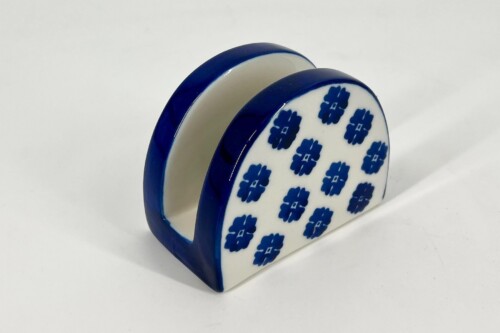 Decorative blue-and-white porcelain piece, showing a circular face with repeating blue floral motifs on white, likely a napkin ring or small dish edge.