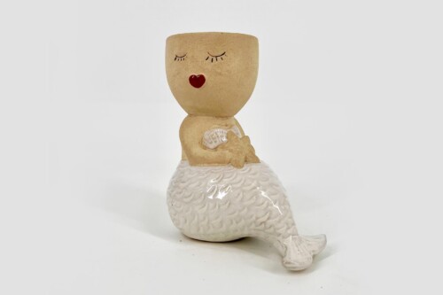 Whimsical ceramic figure of a small head with closed eyes and red lips, sitting on a white mermaid tail