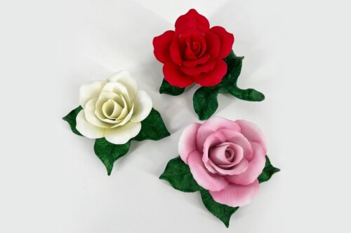 Three artificial roses in red, white, and pink with green leaves on a pale background.