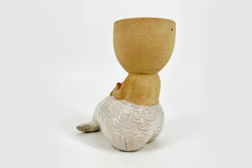 Ceramic figurine of a small person with a tan head sitting on a white textured swan base.
