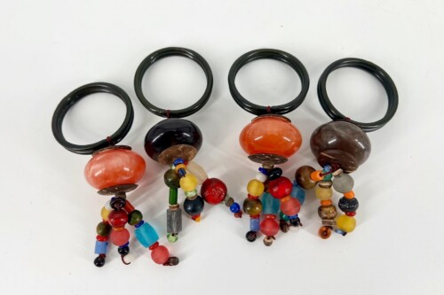 Four black circular bangles each linked to a hanging strand of colorful beads and orange/dark stones, creating a bohemian bracelet set.
