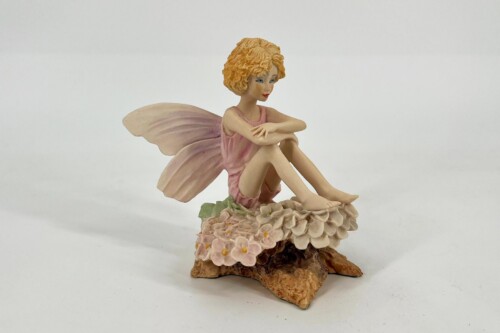 Fairy figurine with pink dress and delicate wings sitting atop a flower-covered base.