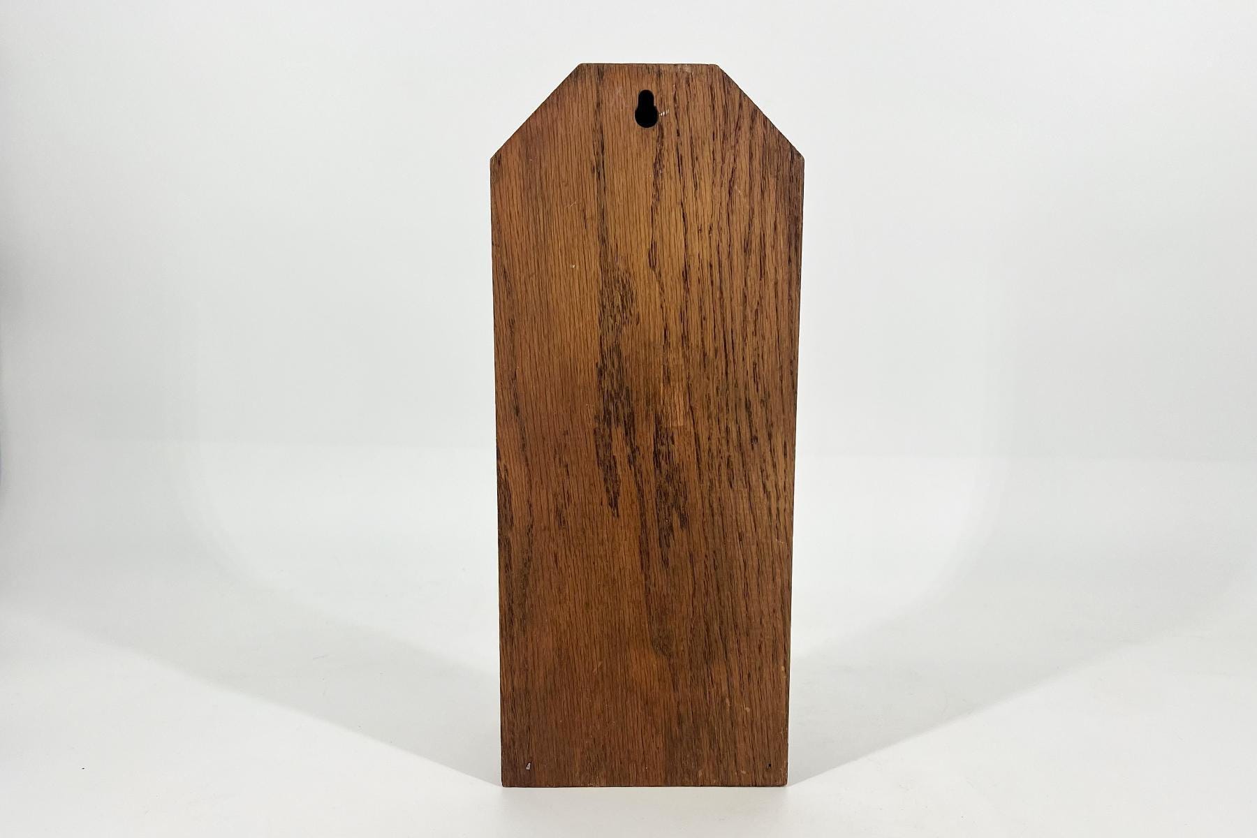 Wooden stake/post with a beveled, pointed top and a small keyhole-shaped hole near the top, standing on a white surface.