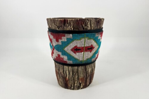 Handcrafted wooden cup wrapped in a colorful geometric beadwork band on a textured stump base