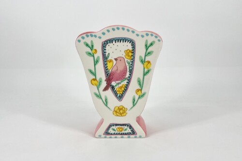 Decorative illustration of a pink bird inside a shield-shaped frame, bordered by blue curls and yellow flowers with green vines on white background.