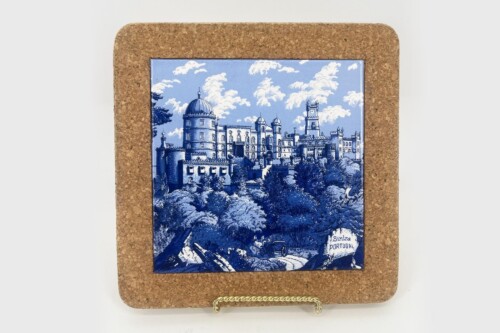 Blue-and-white ceramic tile showing a castle scene mounted on a corkboard frame.