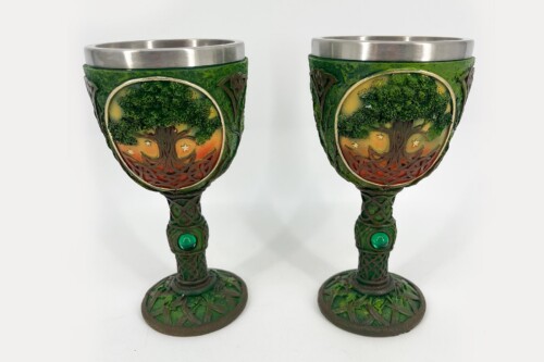 Two ornate green goblets with tree and lattice designs, metal rims, and emerald accents placed side by side.