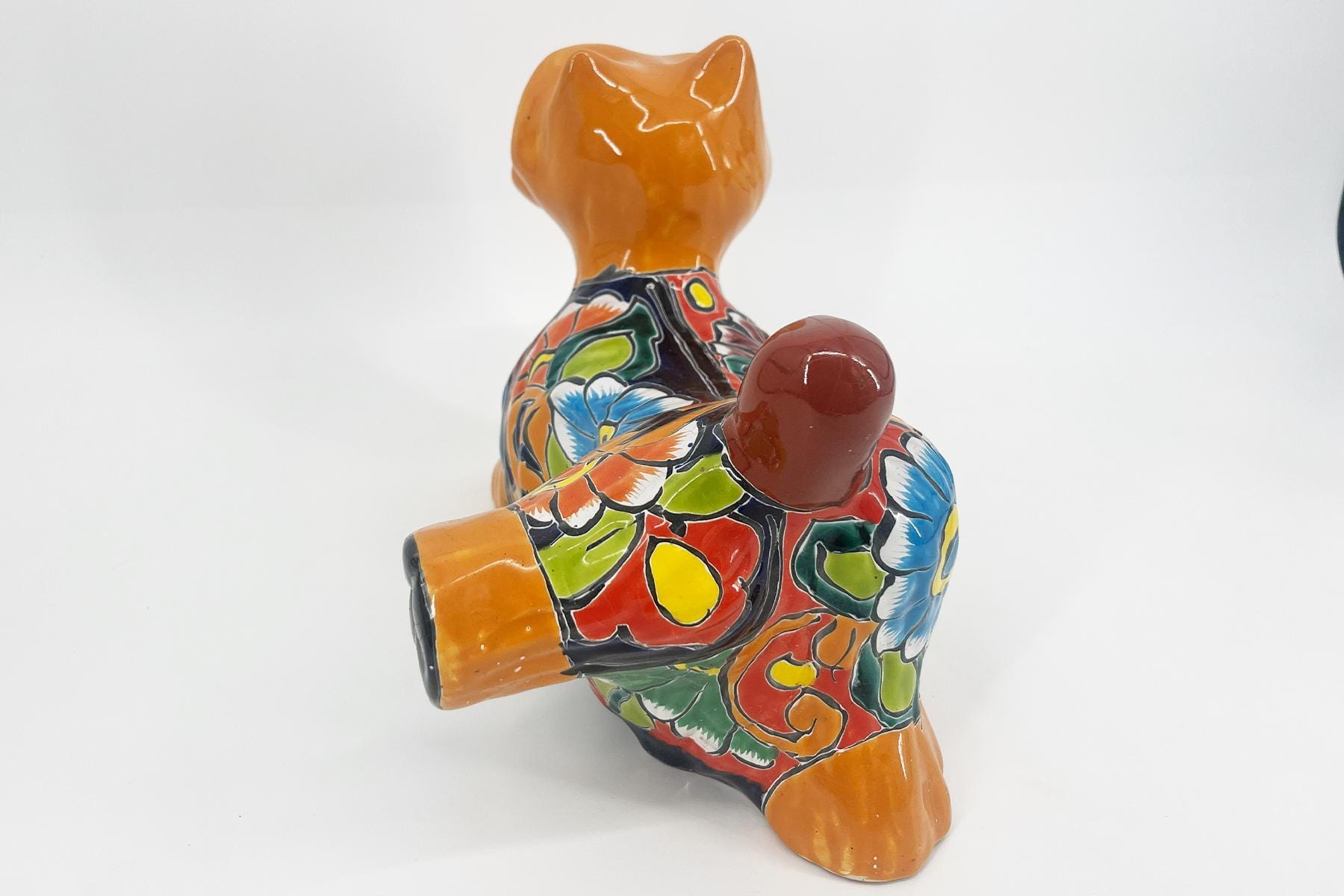 Back view of a colorful ceramic cat figurine with an orange head and tail, covered in a vibrant floral pattern.