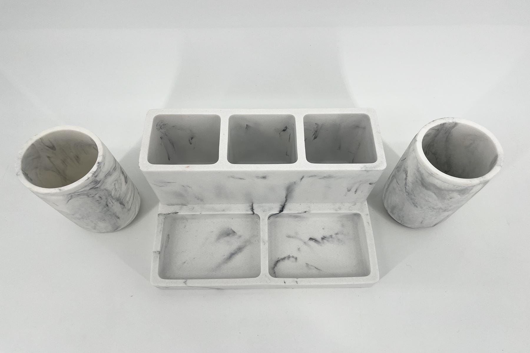 White marble desk organizer with two cylindrical holders on either side and a central three-slot tray with marble-veined surfaces.