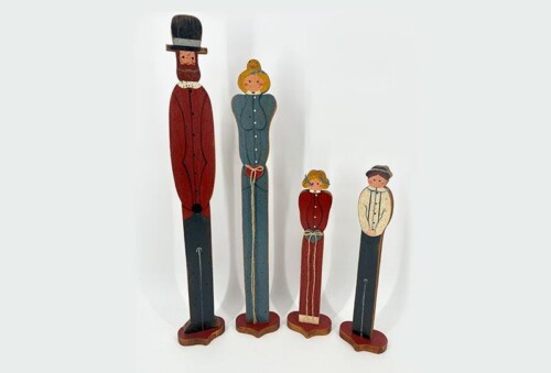 Wooden peg-family figurines standing in a row: father in a red suit with a top hat, mother in a blue dress, and two children in red and cream outfits.