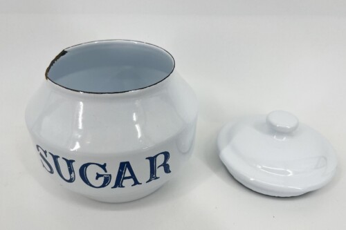 White ceramic sugar jar with blue 'SUGAR' lettering and the lid placed to the side on a white surface.