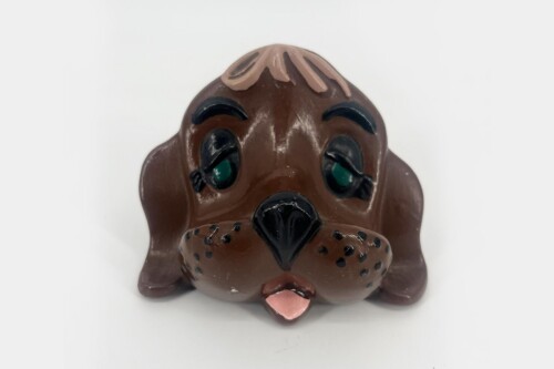 Brown dog-shaped sculpture with a pink tongue, dark nose, and green eyes, facing forward against a light background.