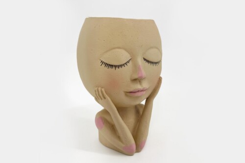 Clay sculpture of a young person with closed eyes, hands cupping the cheeks, pink heart marks on shoulders and chest.