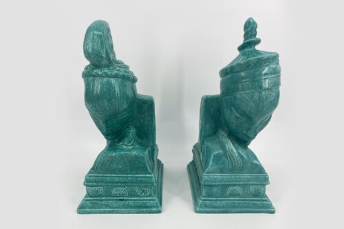 Two turquoise ceramic sculptures of seated figures facing each other, view from behind.