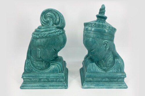 Two turquoise ceramic statues facing each other, each with ornate headdresses and patterned robes on decorative square bases.