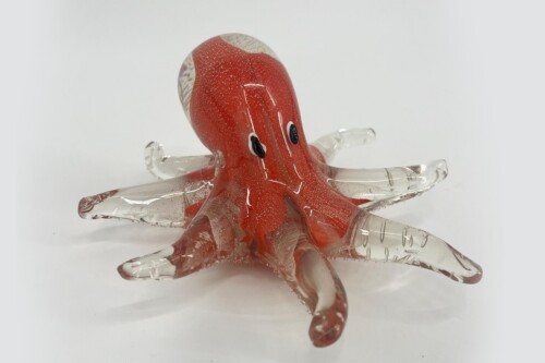 Red glass octopus sculpture with clear, textured tentacles and small black eyes, set against a pale background.