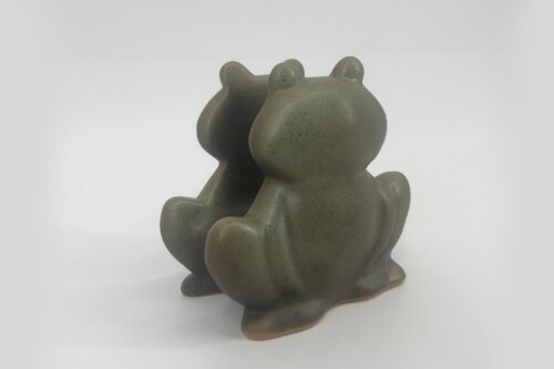 Gray ceramic frog figurine with rounded features, placed on a white surface.