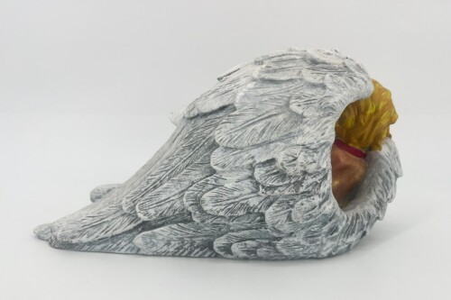 Gray stone angel sculpture lying on its side, wings folded over its back with golden hair peeking out.