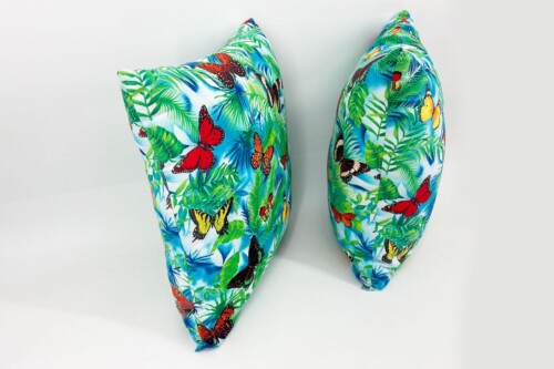 Two tropical-patterned throw pillows with butterfly and palm leaf design against a white background; blue and green colors dominate.