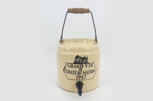 Beige ceramic beverage jug with a wooden handle and metal frame, spigot at bottom, labeled 'Grand Vin de Château Maison 1947' (vintage wine cooler).
