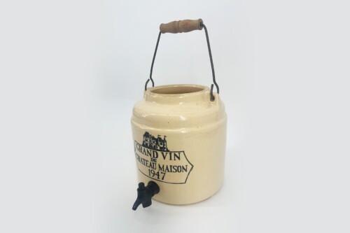 Cream-colored ceramic wine jug with a wooden handle and black spigot, labeled 'Grand Vin de Château Maison 1947'