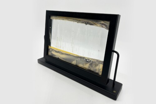 Black rectangular frame on a stand holds an abstract resin piece with gold and gray swirls along a light backdrop.