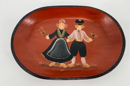 Decorative oval plate featuring a couple in traditional clothing dancing on a red background, holding flowers.