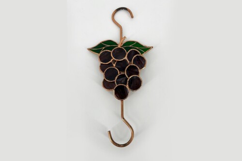 Copper hook shaped like a grapevine with dark glass grape clusters and green leaves at the top of the stem.