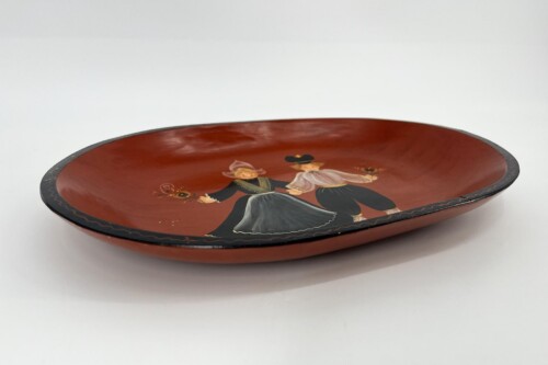 Oval red wooden tray with a painted scene of a man and woman in 19th-century attire dancing, bordered by a black rim with a wavy decorative edge