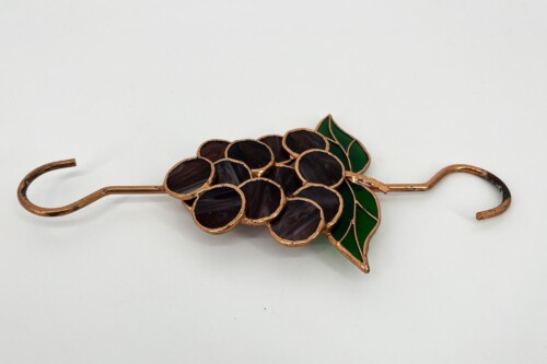 Copper-colored metal wall hook shaped like a grape bunch with dark purple glass cells and green leaves in the design.