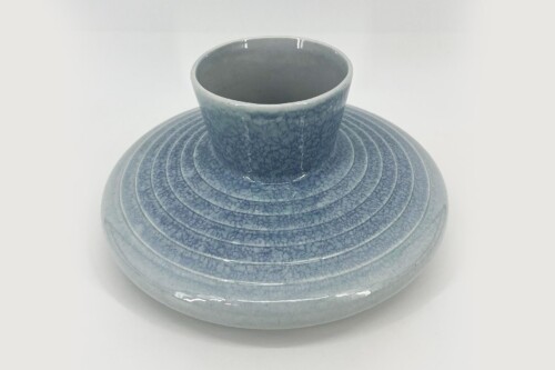 Blue glazed ceramic vase with a narrow neck sitting on a round, ribbed base or pedestal with concentric rings.