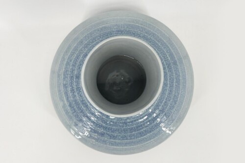 Top-down view of a blue ceramic plate with a smaller matching bowl centered on a white surface, showing concentric ridges and glaze crackle patterns.
