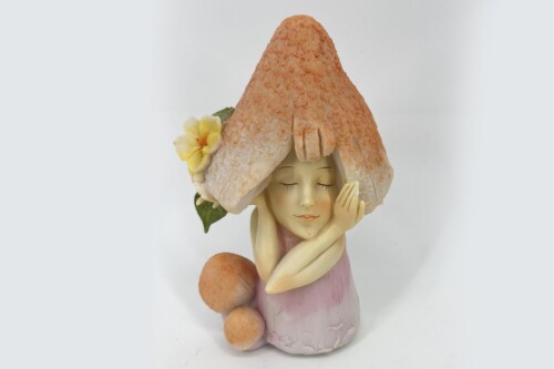 Ceramic statue of a girl with a large peach-colored mushroom hat, yellow flower, and peaches at her side and hands folded near her face.